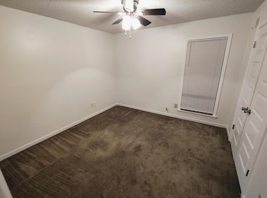 Spare room featuring dark colored carpet, a ceiling fan, baseboards, and a textured ceiling
