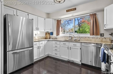 Kitchen with stainless steel appliances, white cabinets, dark wood-type flooring, and light stone countertops