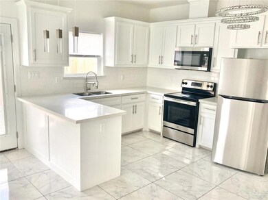 Kitchen with stainless steel appliances, light marble finish floors, a peninsula, white cabinets, and light countertops