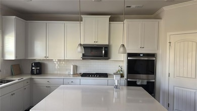 Kitchen featuring stainless steel appliances, white cabinetry, tasteful backsplash, light stone counters, and crown molding