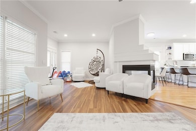 Living area with ornamental molding, light wood-type flooring, a multi sided fireplace, and recessed lighting