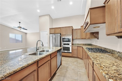 Kitchen with stainless steel appliances, light stone counters, ceiling fan, lofted ceiling, and light tile patterned floors