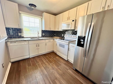 Kitchen featuring white appliances, tasteful backsplash, white cabinets, dark wood finished floors, and light stone countertops