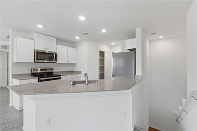 Kitchen with light stone countertops, stainless steel appliances, white cabinets, recessed lighting, and light wood-style floors