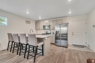 Kitchen with gray cabinetry, appliances with stainless steel finishes, a breakfast bar, light wood-style floors, and recessed lighting