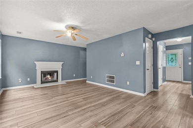 Unfurnished living room featuring a ceiling fan, a textured ceiling, light wood-type flooring, and a lit fireplace