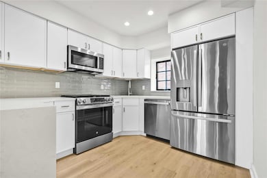 Kitchen with stainless steel appliances, light countertops, light wood-type flooring, backsplash, and white cabinets