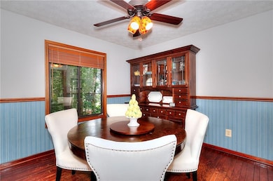 Dining space with dark wood-style floors, wainscoting, a textured ceiling, ceiling fan, and wallpapered walls