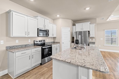 Kitchen featuring appliances with stainless steel finishes, white cabinets, light wood-style flooring, a center island with sink, and recessed lighting