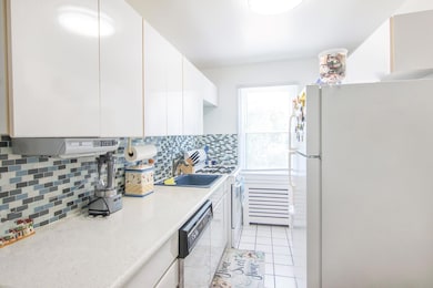 Kitchen featuring white appliances, decorative backsplash, light countertops, white cabinetry, and light tile patterned floors