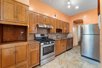 Kitchen with stainless steel appliances, decorative backsplash, brown cabinets, under cabinet range hood, and arched walkways