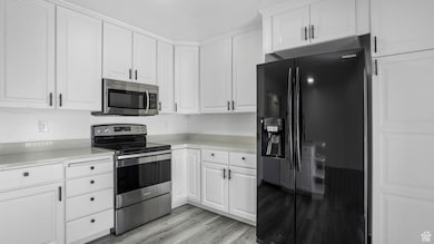 Kitchen featuring stainless steel appliances, white cabinets, light countertops, and light wood-type flooring