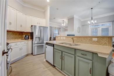 Kitchen with white cabinets, an accented green island with sink, appliances with stainless steel finishes, crown molding, and a dishwasher