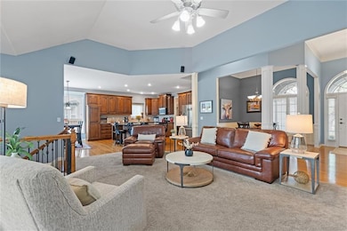 Living room with light wood-style flooring, a chandelier, ceiling fan, lofted ceiling, and decorative columns