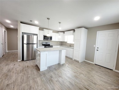 Kitchen with stainless steel appliances, a kitchen island, pendant lighting, white cabinetry, and light wood-type flooring