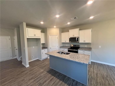 Kitchen featuring appliances with stainless steel finishes, a kitchen island with sink, dark wood-type flooring, white cabinetry, and recessed lighting