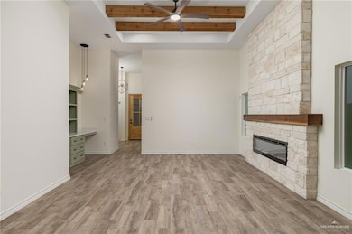 Unfurnished living room with a fireplace, ceiling fan with notable chandelier, wood-style flooring, and beamed ceiling