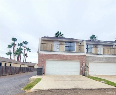 View of front facade with brick siding, driveway, central AC unit, a garage, and a balcony