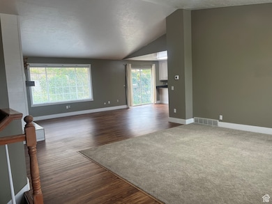 Unfurnished living room featuring dark wood-style flooring, lofted ceiling, and a textured ceiling