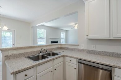 Kitchen with dishwasher, a sink, white cabinets, a fireplace, and light countertops