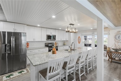 Kitchen featuring stainless steel appliances, a breakfast bar area, tasteful backsplash, light stone counters, and a center island with sink