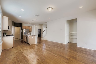 Kitchen with open floor plan, hanging light fixtures, light wood-style floors, light stone counters, and recessed lighting