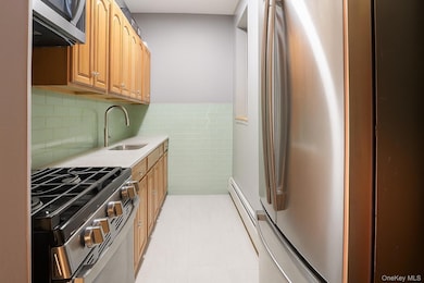 Kitchen with appliances with stainless steel finishes, tile walls, brown cabinets, light tile patterned floors, and a baseboard radiator