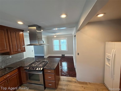Kitchen with stainless steel range with gas stovetop, white fridge with ice dispenser, island exhaust hood, dark stone countertops, and backsplash