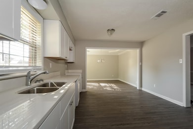 Kitchen with white cabinets, dark wood-style flooring, light stone counters, a chandelier, and decorative light fixtures