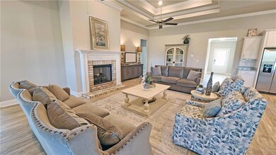 Living area featuring a tray ceiling, light wood-style floors, crown molding, a fireplace, and ceiling fan