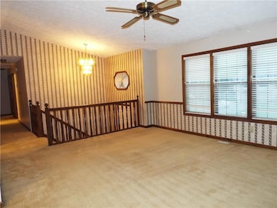 Spare room featuring wallpapered walls, carpet floors, a ceiling fan, and a chandelier