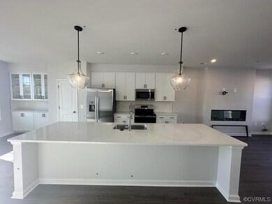 Kitchen with white cabinets, appliances with stainless steel finishes, a kitchen island with sink, and dark wood-type flooring