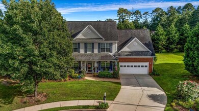 Traditional-style house with an attached garage, a porch, a front yard, driveway, and brick siding