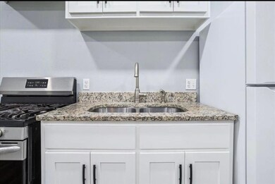 Kitchen featuring stainless steel range with gas stovetop, freestanding refrigerator, white cabinets, and light stone countertops
