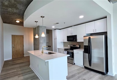 Kitchen featuring stainless steel appliances, a sink, light wood-style floors, backsplash, and white cabinetry