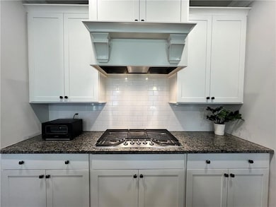 Kitchen featuring premium range hood, stainless steel gas cooktop, white cabinets, and backsplash
