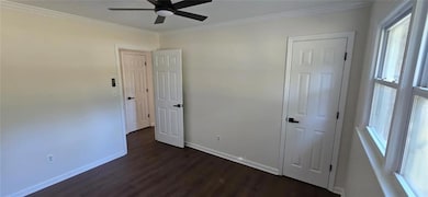 Unfurnished bedroom featuring dark wood-type flooring, crown molding, and ceiling fan