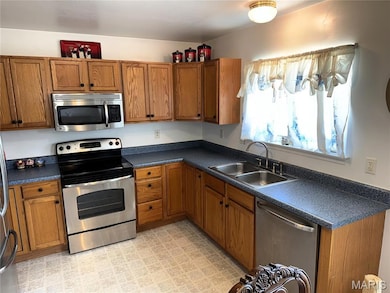 Kitchen with stainless steel appliances, dark countertops, brown cabinetry, and light flooring