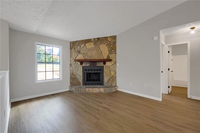 Unfurnished living room featuring wood finished floors, a textured ceiling, and a stone fireplace