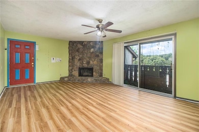 Unfurnished living room featuring a textured ceiling, wood finished floors, a ceiling fan, and a stone fireplace