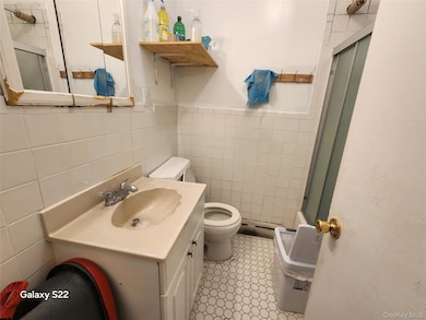 Bathroom with toilet, tile walls, an enclosed shower, vanity, and wainscoting
