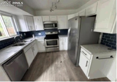 Kitchen with appliances with stainless steel finishes, a sink, backsplash, white cabinetry, and light wood-style floors
