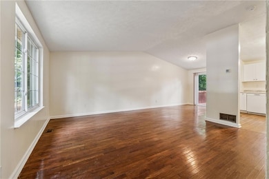 Unfurnished living room with dark wood-style flooring, vaulted ceiling, and a textured ceiling