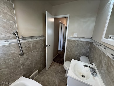 Full bath with tile walls, vanity, and wainscoting