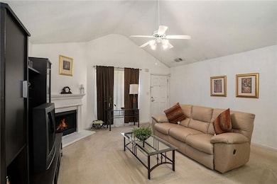 Living area featuring light colored carpet, lofted ceiling, a ceiling fan, and a lit fireplace