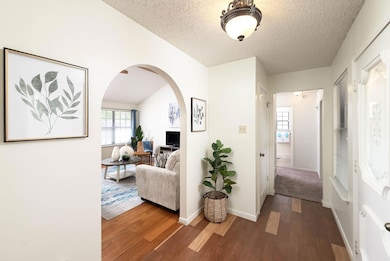 Corridor with arched walkways, dark wood-type flooring, plenty of natural light, and a textured ceiling