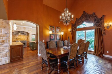 Surrounded by gently arched openings to the living space, this elegant dining room showcases an ornate iron & crystal chandelier suspended from the 14' cathedral ceiling that frames the large front-facing palladium arched window dressed with custom draperies.