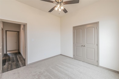 Unfurnished bedroom with dark colored carpet, ceiling fan, and a closet