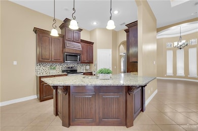 Kitchen featuring light stone counters, hanging light fixtures, arched walkways, appliances with stainless steel finishes, and recessed lighting