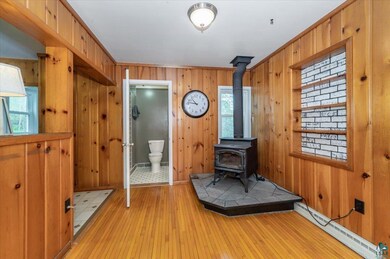 Foyer entrance featuring baseboard heating, a wood stove, wooden walls, and light wood-style floors